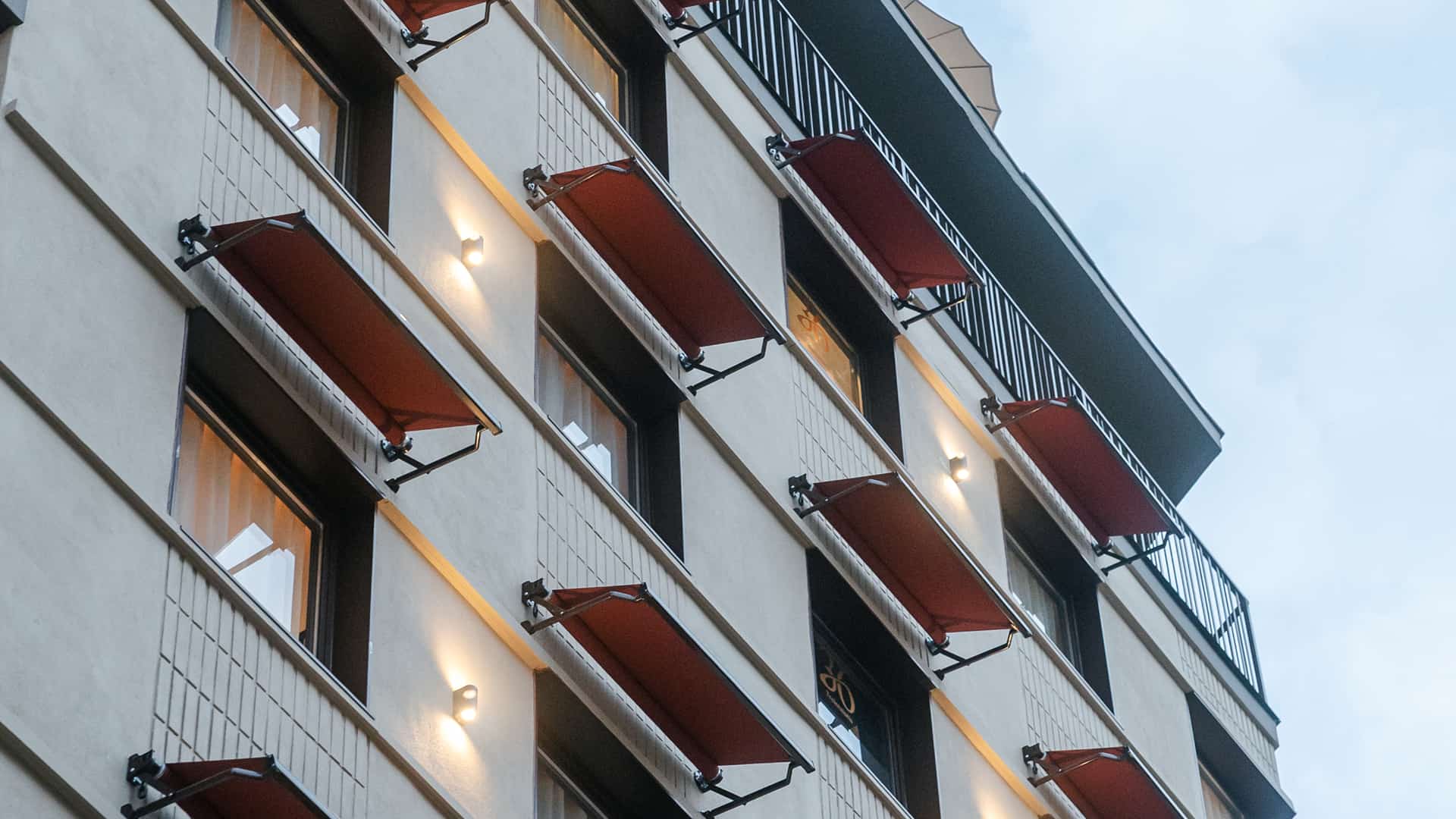 Fachada con toldos rojos Fachada de un edificio con toldos rojos en los balcones y apliques de luz encendidos bajo el cielo azul