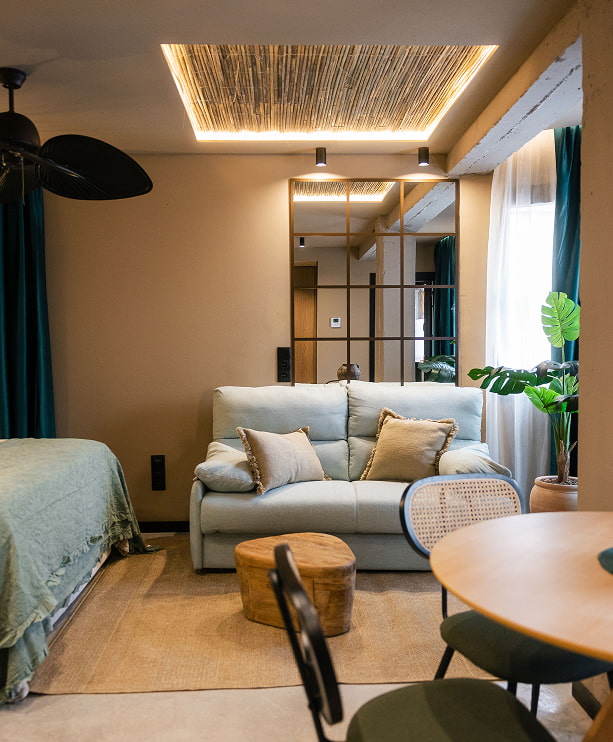 Estudio con cama, sofá, mesa baja de madera y techo de cañizo iluminado en un apartamento turístico de Murcia