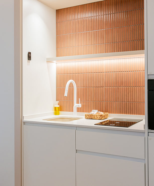 Cocina con placa de inducción, fregadero y pared de azulejos color terracota en un apartamento turístico de Grupo CCOMMO