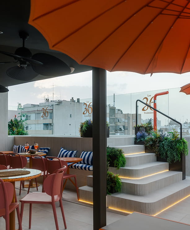 Azotea con sombrillas naranjas, sillas y escalera iluminada en unos apartamentos en el centro de Murcia