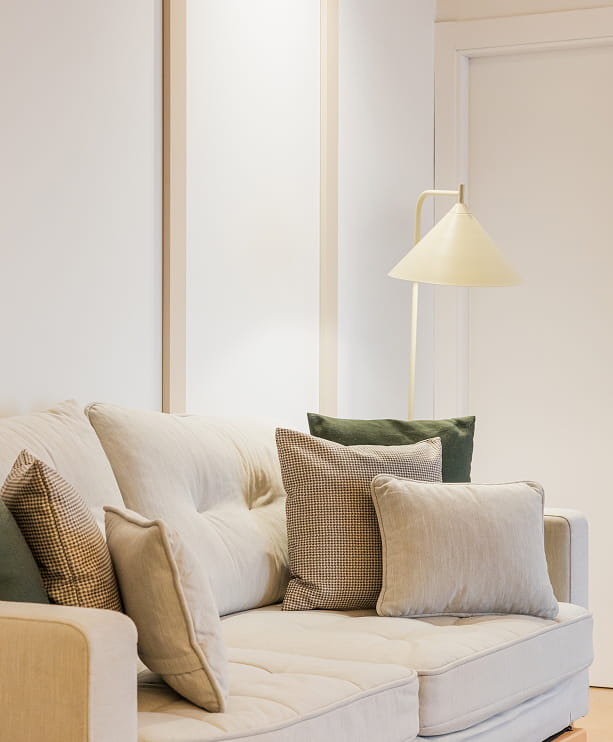 Salón de un apartamento turístico en Murcia con sofá claro, cojines de cuadros y lámpara de pie