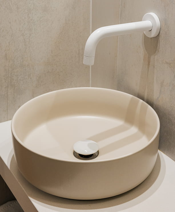 Lavabo redondo color crema con grifo blanco empotrado en una pared de piedra clara