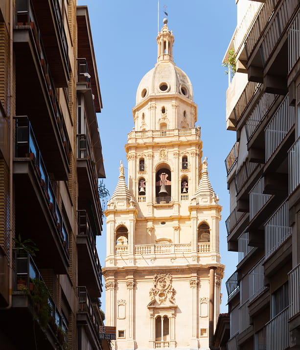 Calle del centro de Murcia con la torre barroca de la Catedral al fondo, entre balcones y fachadas