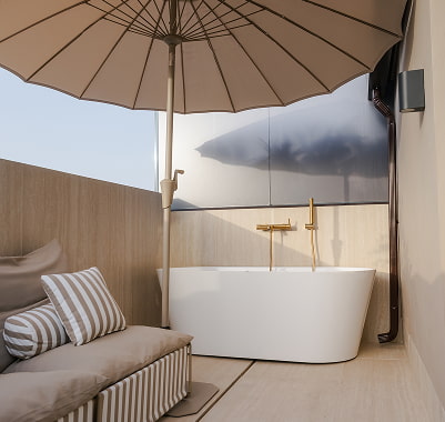Terraza de un apartamento en el centro de Murcia con bañera exenta, sofá con cojines de rayas y sombrilla