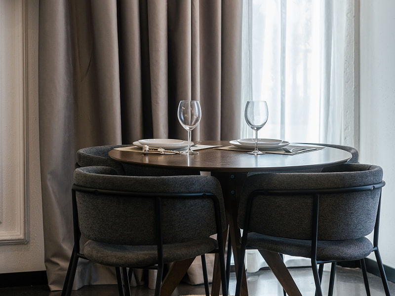 Apartamento Premium con balcón | Comedor Mesa redonda de comedor con dos copas, platos y sillas tapizadas junto a cortinas grises