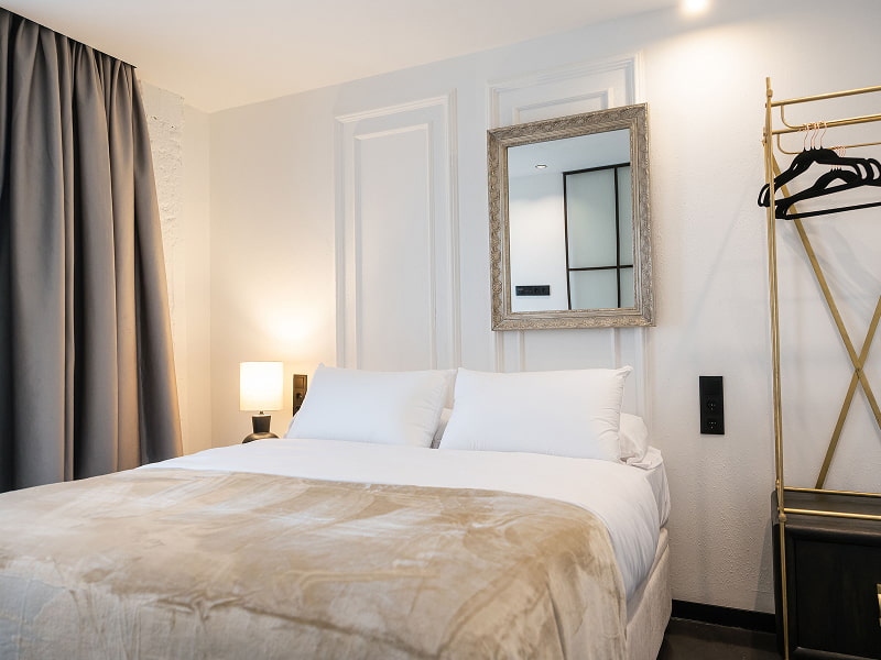 Apartamento Premium con balcón | Vista del dormitorio Dormitorio con cama doble, manta beige, perchero dorado y cortinas grises