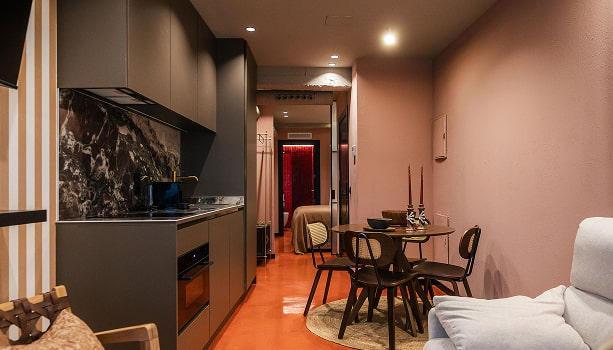 Apartamento Premium | Cocina y comedor Cocina gris con frente de mármol oscuro, suelo terracota y comedor con mesa redonda junto a paredes rosadas