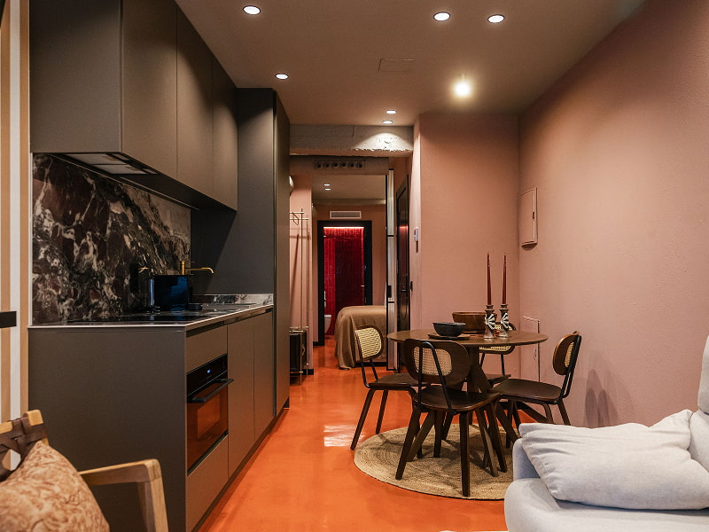 Apartamento Premium | Cocina y comedor Cocina gris con frente de mármol oscuro, suelo terracota y comedor con mesa redonda junto a paredes rosadas