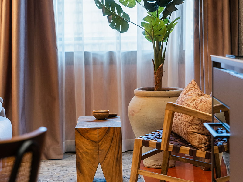 Apartamento Premium | Zona de estar Butaca de madera con cojín estampado, mesita auxiliar y planta junto a una ventana con cortinas