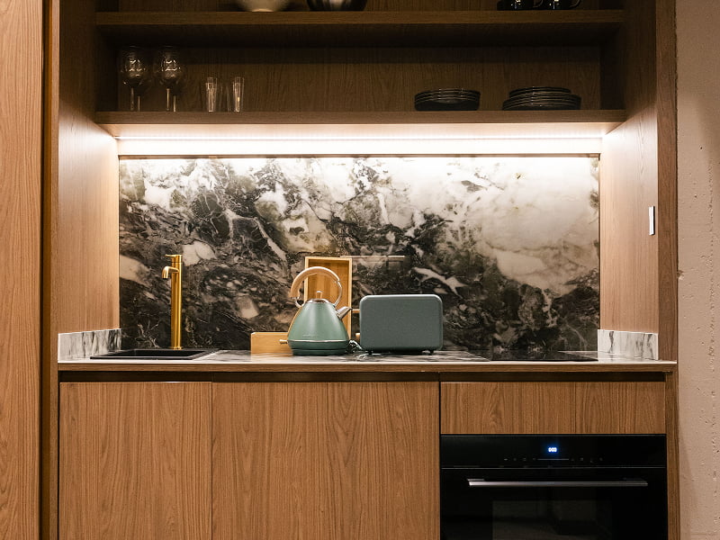 Apartamento Premium | Cocina Cocina de madera con frente de mármol, horno, hervidor y estante iluminado con vajilla