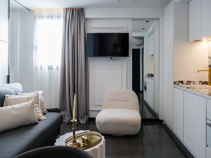 Apartamento Premium | Salón y cocina Salón con sofá, butaca blanca y televisión, con la cocina blanca a lo largo de la pared