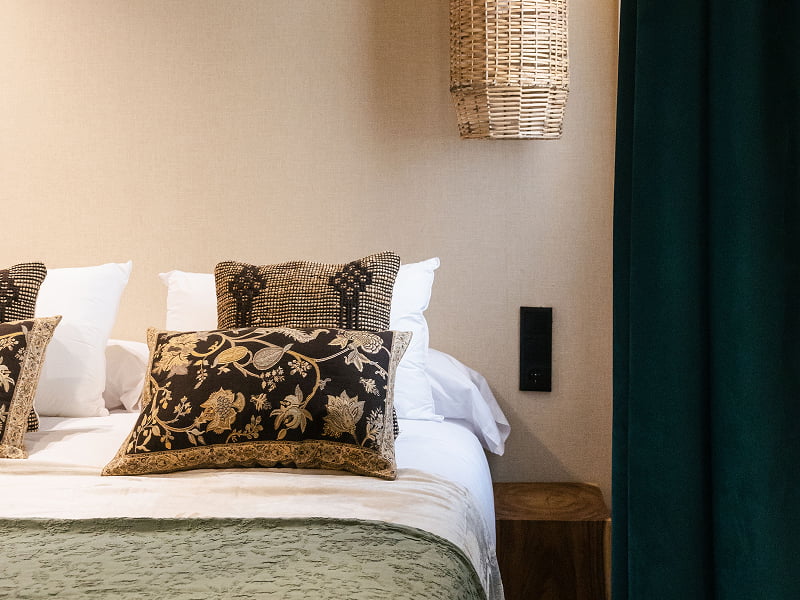 Apartamento Premium | Cama Cama con cojines estampados en tonos oscuros, aplique de mimbre y cortina verde