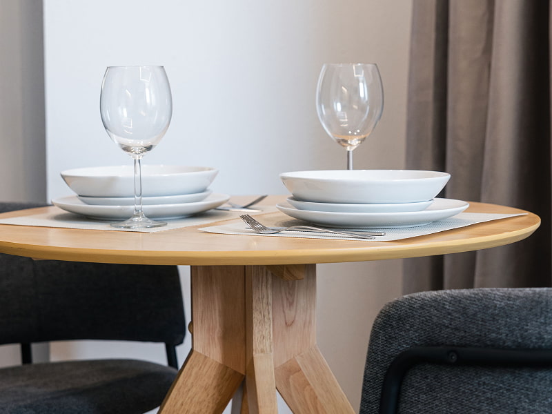 Apartamento para 2 | Comedor Mesa redonda de madera puesta para dos, con copas de vino y sillas grises