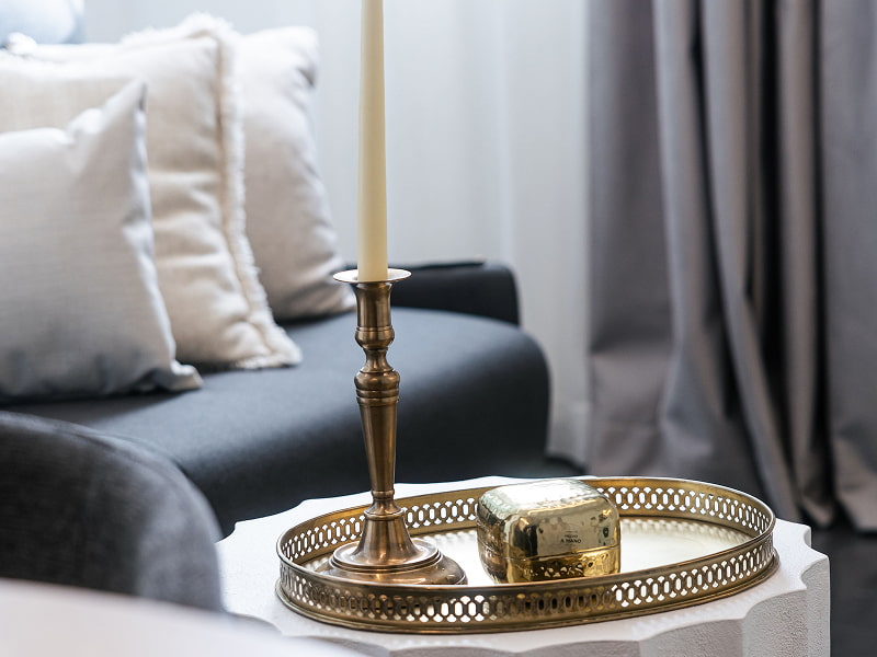 Apartamento para 2 | Detalle decorativo Bandeja dorada con candelabro y vela sobre una mesa blanca junto al sofá