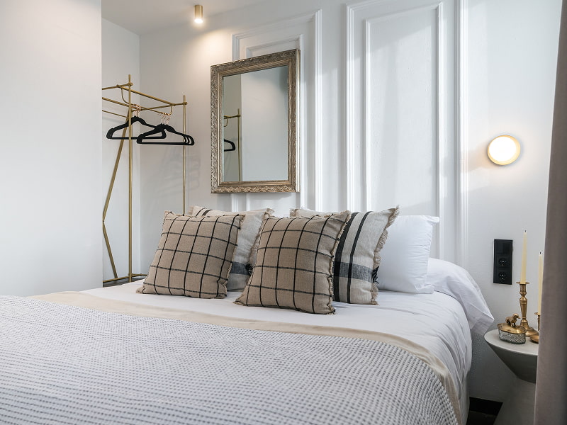 Ático con vistas | Dormitorio Dormitorio con cama doble, cojines de cuadros, espejo de marco plateado y perchero dorado
