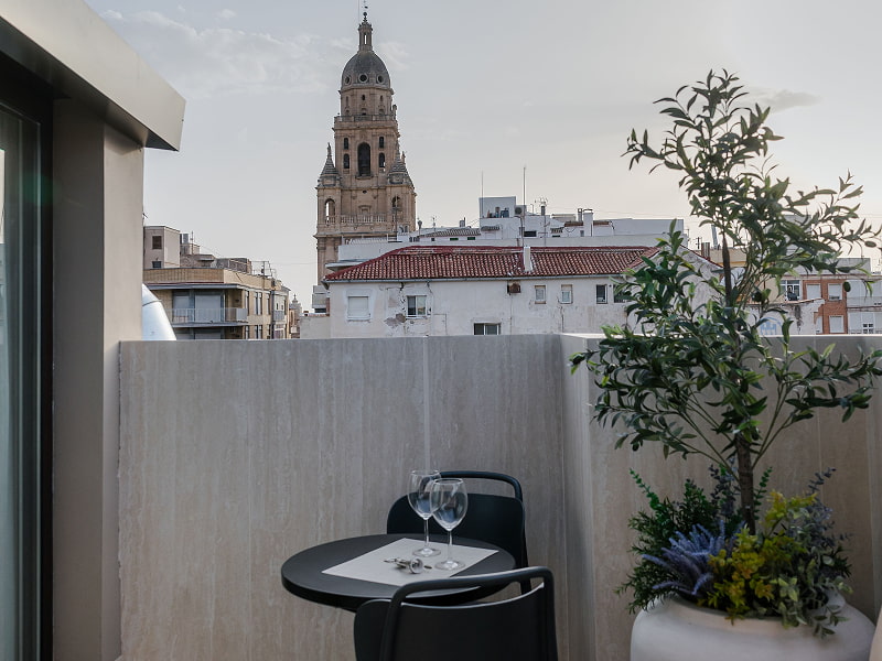 Ático con vistas | Terraza con vistas Terraza con mesa para dos, copas y olivo frente a la torre de la Catedral de Murcia