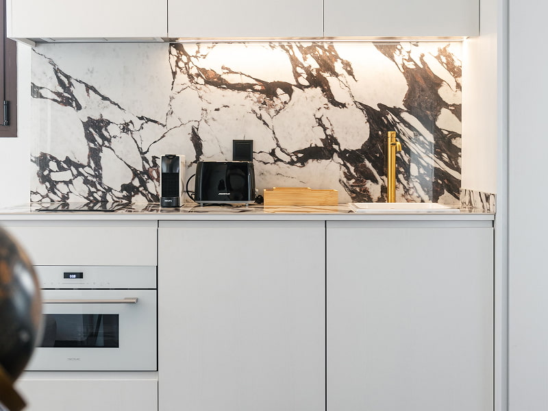 Ático con vistas | Cocina Cocina blanca con horno integrado, grifo dorado y frente de mármol veteado en blanco y negro