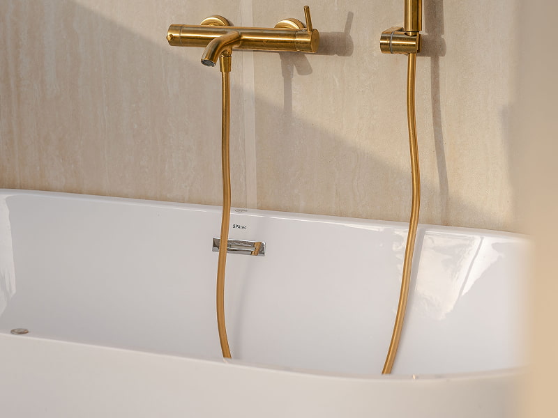 Ático con vistas | Detalle del jacuzzi Grifería y ducha de mano doradas sobre la bañera blanca del jacuzzi