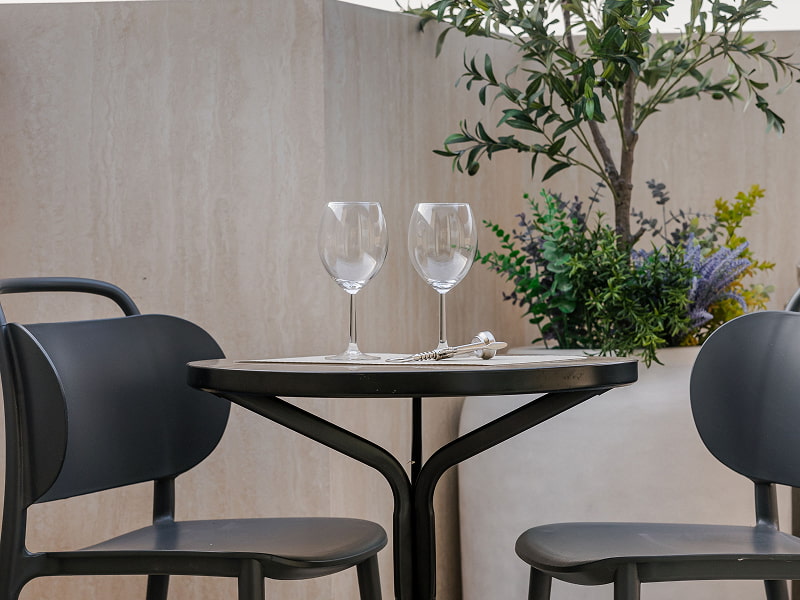 Ático con vistas | Mesa en la terraza Mesa redonda negra con dos copas y sillas a juego entre plantas en la terraza del ático