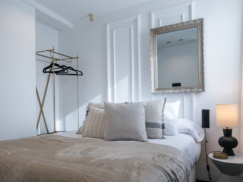 Penthouse with hot tub | Dormitorio Cama doble con cojines grises, espejo de marco plateado, lámpara negra y perchero dorado