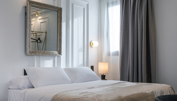 Estudio Premium con balcón | Dormitorio Cama doble con manta beige, espejo de marco plateado, aplique y cortinas grises