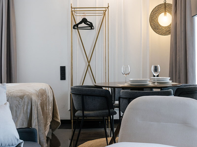Estudio Premium con balcón | Comedor Mesa redonda con copas y sillas negras junto a un perchero dorado y una lámpara de mimbre