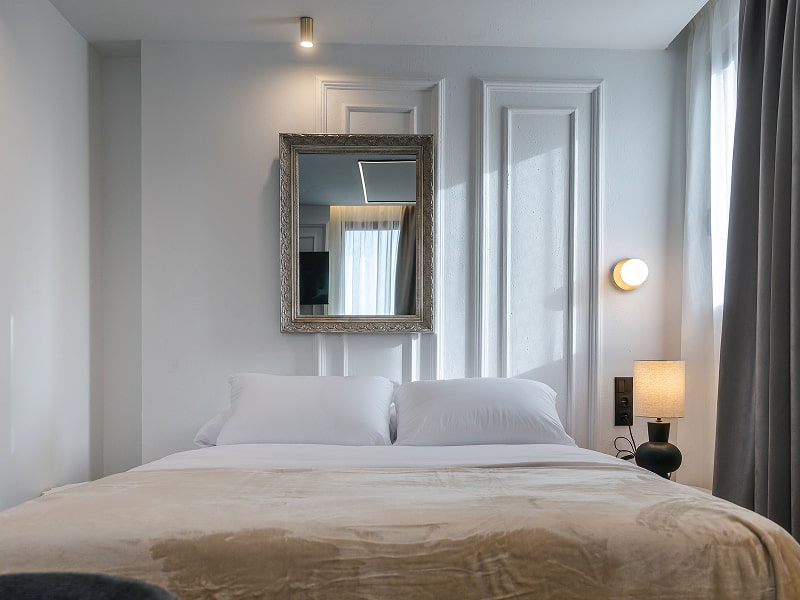 Estudio Premium con balcón | Cama Cama doble frente a una pared con molduras, espejo plateado y lámpara de mesilla
