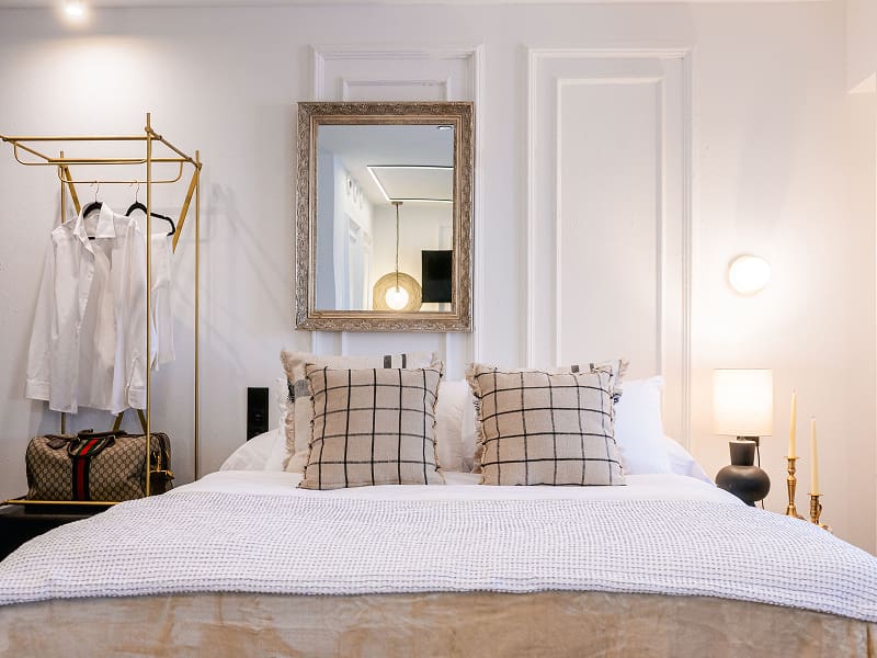 Estudio Premium | Dormitorio Cama doble con cojines de cuadros, espejo plateado y perchero dorado con camisas