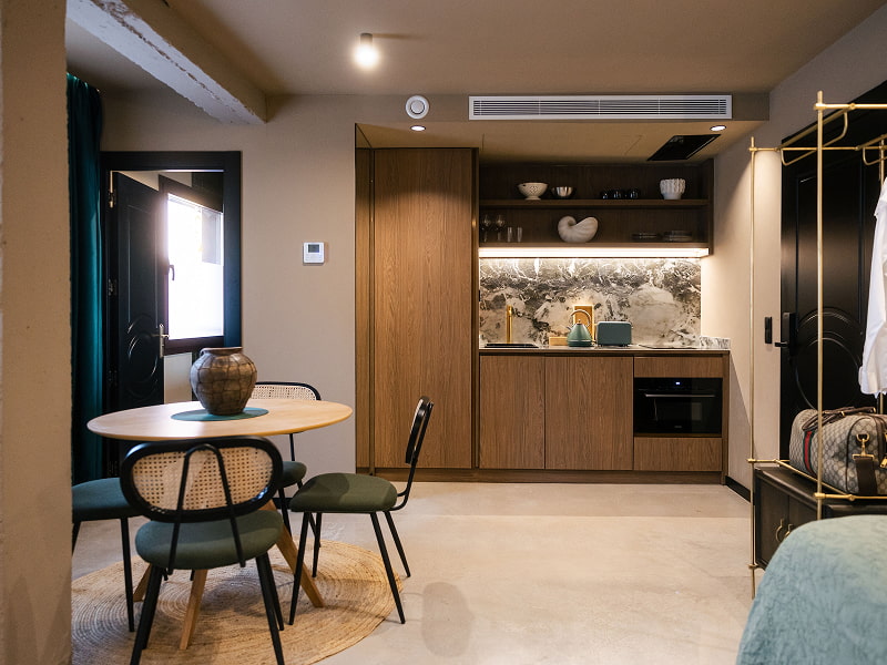 Estudio Premium | Comedor y cocina Mesa redonda con sillas verdes y jarrón de cerámica frente a la cocina de madera