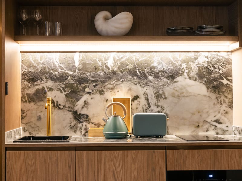 Estudio Premium | Cocina Cocina con frente de mármol, hervidor, tostadora, grifo dorado y estante iluminado con copas