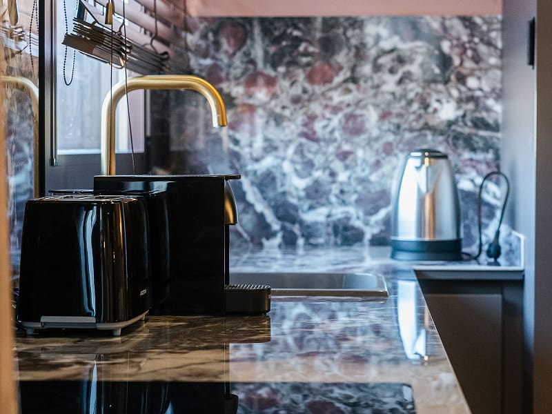 Estudio Premium | Detalle de la cocina Encimera de mármol oscuro con tostadora, hervidor y grifo dorado