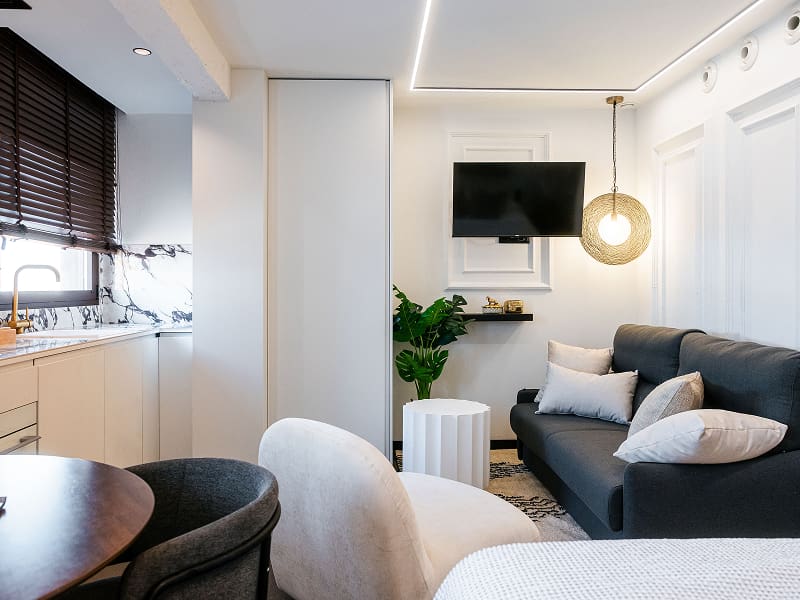Estudio Premium | Salón Sofá gris con cojines, butaca blanca, televisión y lámpara de mimbre colgante