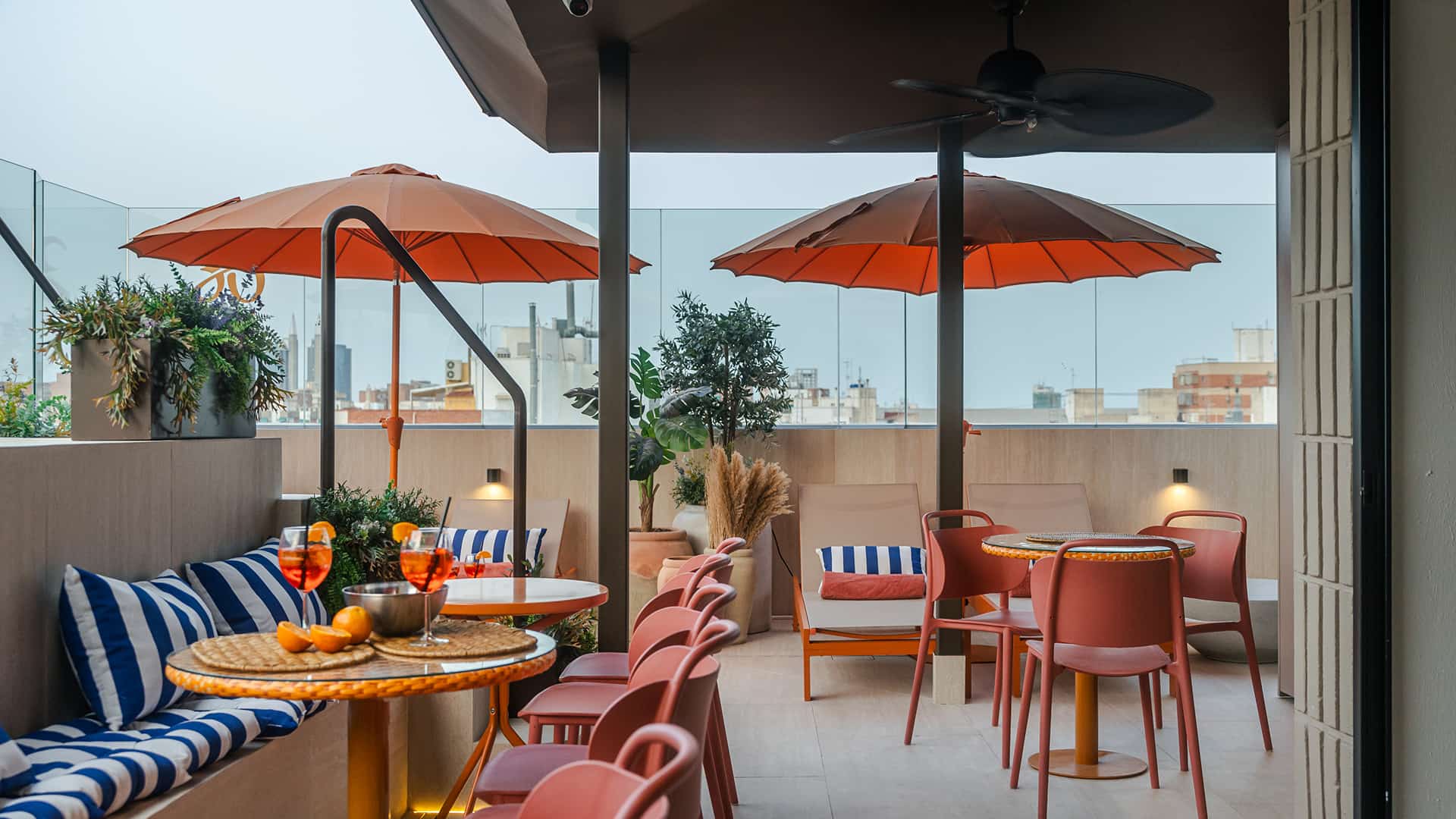 Terraza en la azotea Azotea de Los 36 by Grupo CCOMMO con sombrillas naranjas, mesas, sillas y bancos con cojines de rayas