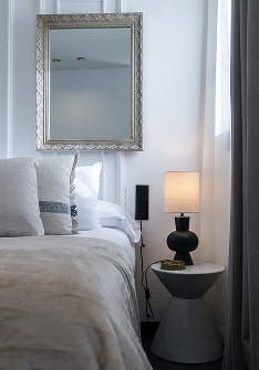 Decoración de estilo París Dormitorio blanco con molduras, espejo de marco plateado y lámpara negra en la mesilla