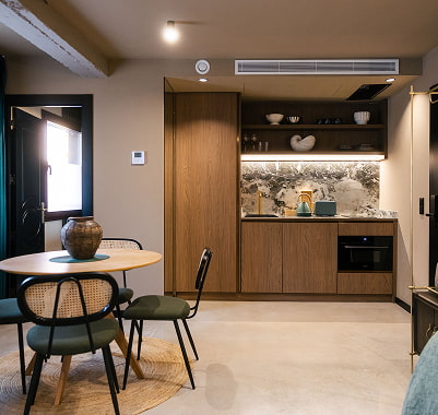 Salón amplio y luminoso Salón con sofá, butaca blanca y suelo oscuro, con amplio espacio de paso hacia la cocina