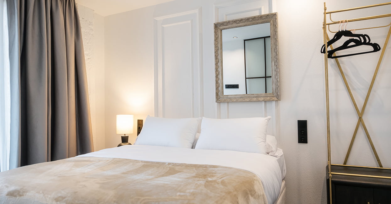 Dormitorio con perchero dorado Dormitorio de Los 36 by Grupo CCOMMO con cama doble, espejo plateado y perchero dorado