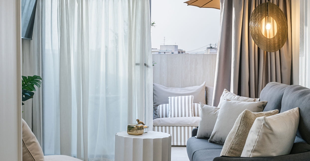Salón con luz natural Salón con sofá gris, cojines claros, lámpara de mimbre y mesa auxiliar blanca junto a la ventana