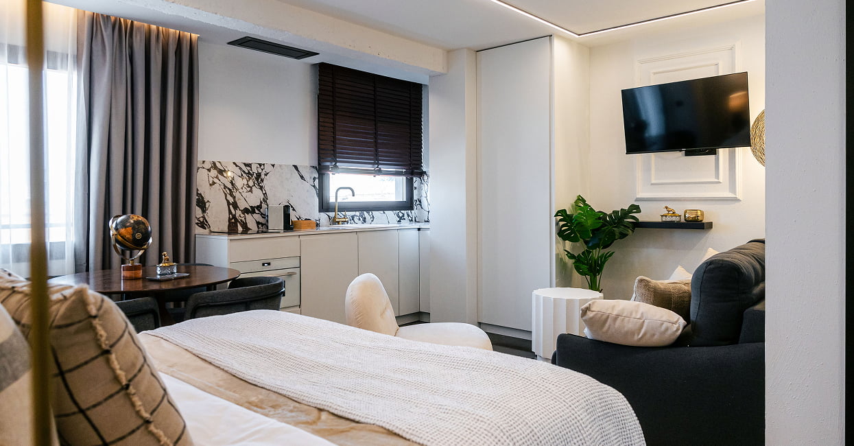Dormitorio y zona de estar Cama, sofá oscuro, televisión y cocina en un espacio abierto y luminoso de Los 36