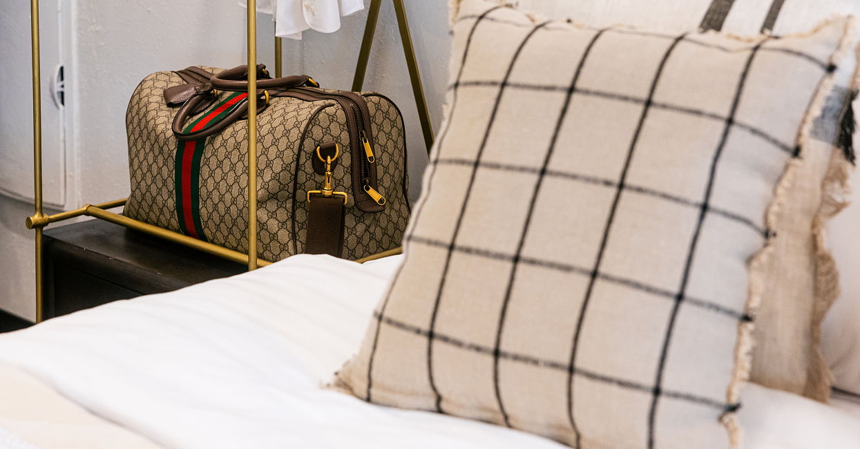 Cama con cojín de cuadros Cojín de cuadros sobre la cama, con una bolsa de viaje en el portaequipajes