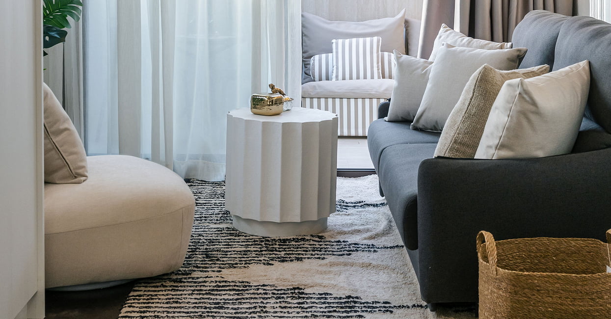 Salón moderno y acogedor con sofá gris Salón moderno con sofá gris, sillón beige, mesa auxiliar blanca, cojines decorativos y alfombra de estilo contemporáneo.