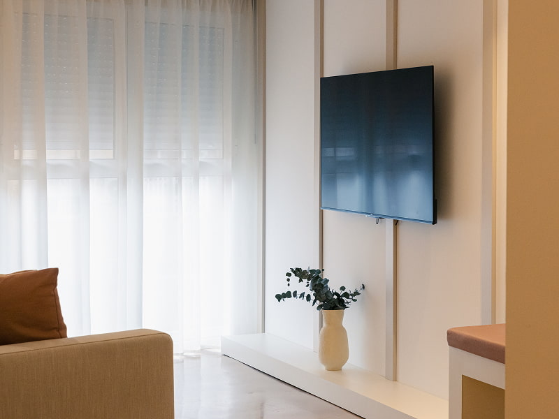 Apartamento 1 habitación | Zona de televisión Rincón del salón con televisión de pared, cortinas blancas y butaca beige