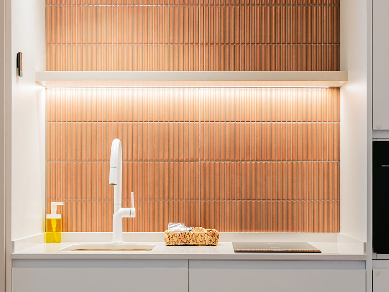 Apartamento 1 habitación | Cocina Cocina con grifo blanco, cesta con utensilios y frente de azulejos terracota con luz LED