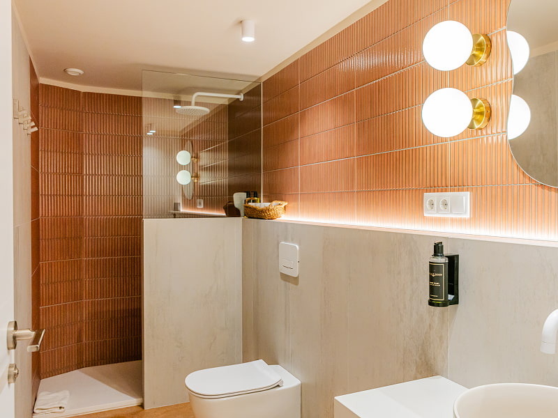 Apartamento 1 habitación | Baño Baño con ducha de azulejos terracota, apliques de globo y encimera de piedra clara