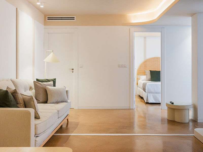 Apartamento 2 habitaciones | Salón Salón con sofá claro y cojines verdes, con vista a uno de los dormitorios por la puerta abierta