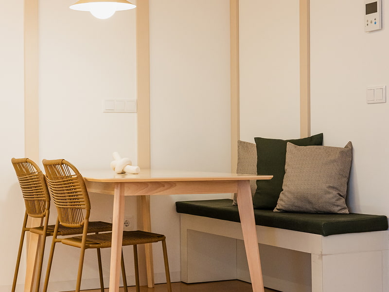 Apartamento 2 habitaciones | Rincón comedor Mesa de madera con sillas de ratán y banco con cojines verdes y grises