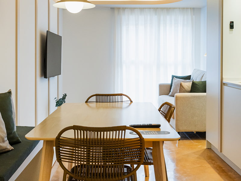 Apartamento 2 habitaciones | Comedor Mesa de comedor alargada con sillas de ratán, televisión en la pared y sofá al fondo