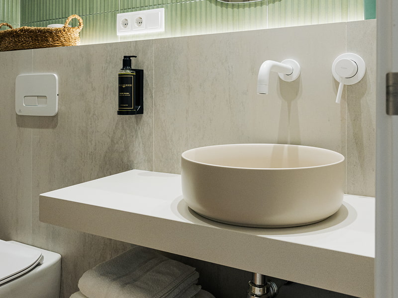 Apartamento 2 habitaciones | Lavabo Lavabo redondo sobre encimera blanca con grifería de pared y toallas bajo la balda