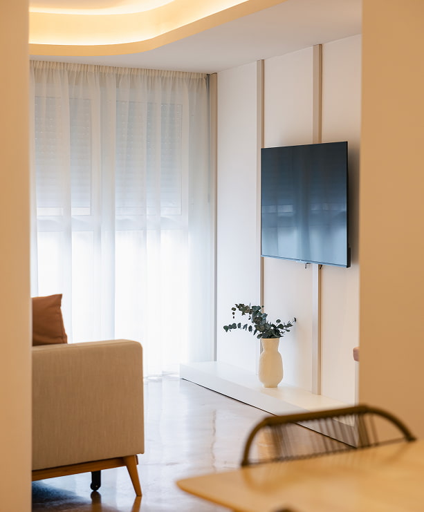Salón con televisión y luz natural Salón luminoso con televisión en la pared, cortinas claras y butaca junto a la ventana