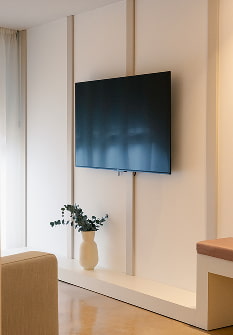 Salón con televisión Pared con televisión, mueble bajo blanco y jarrón con ramas junto a una butaca