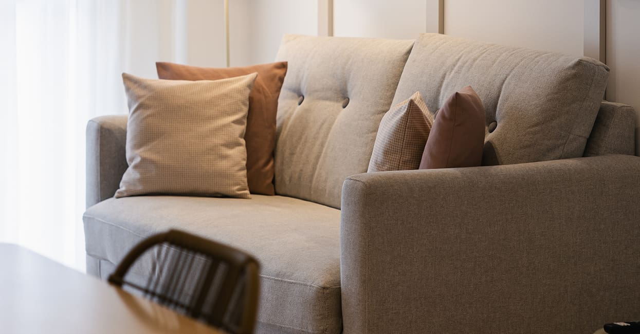 Sofá con cojines en tonos tierra Sofá tapizado en beige con cojines rosas y una silla de ratán en primer plano